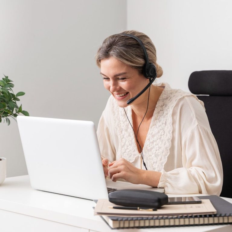 Frau mit Headset lächelt beim Arbeiten am Laptop in einem modernen Büro.