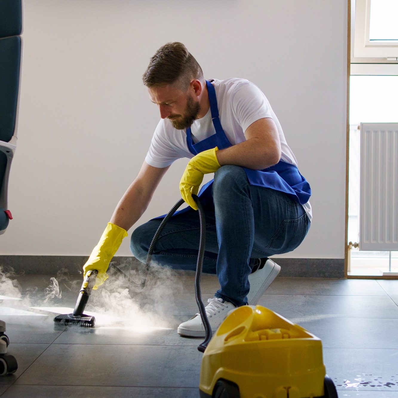 Mann mit gelben Handschuhen reinigt den Boden mit einem Dampfreiniger.