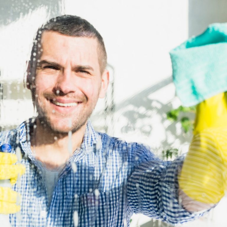 Mann mit Handschuhen putzt ein Fenster und lächelt dabei.