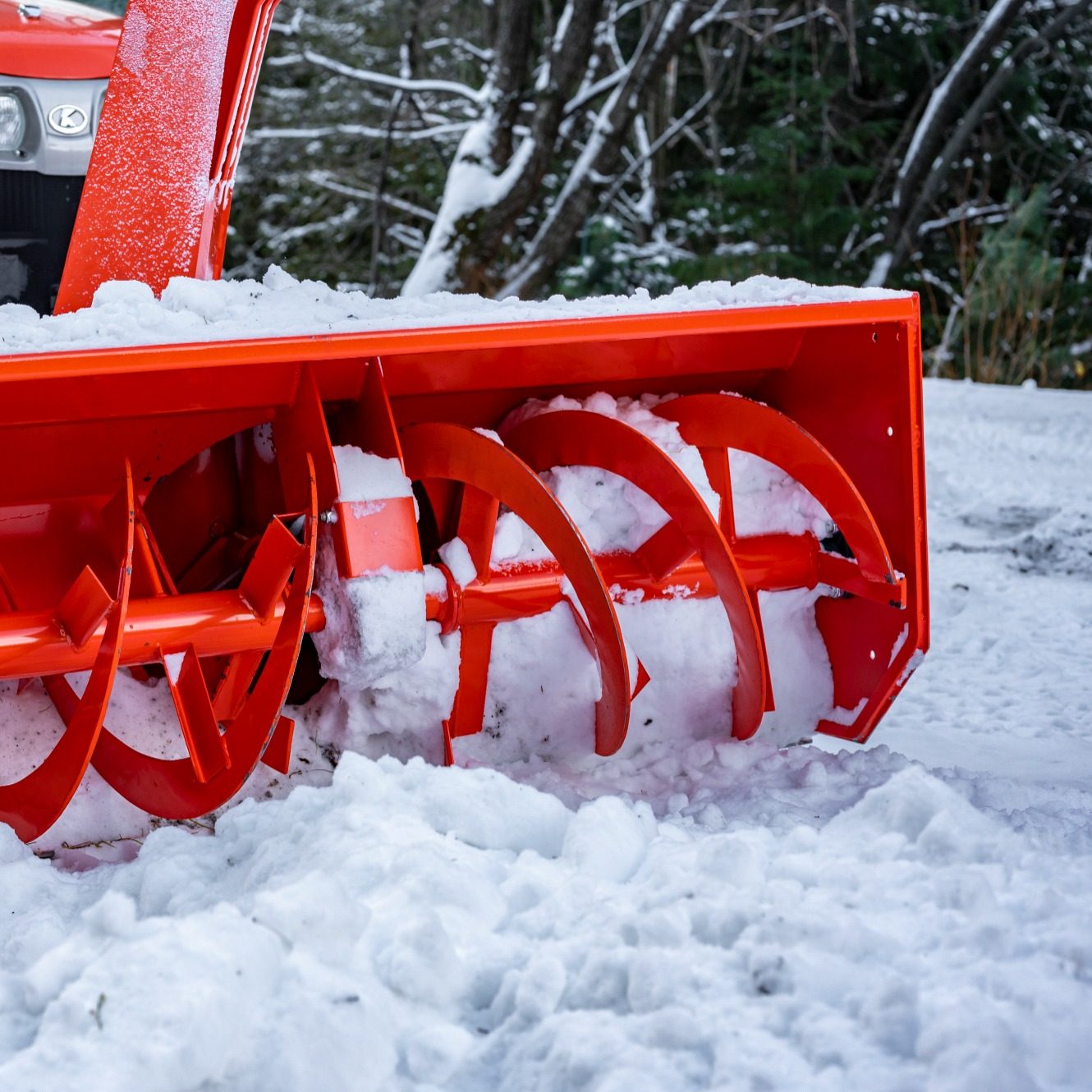 Rote Schneefräse entfernt Schnee auf einem verschneiten Weg.